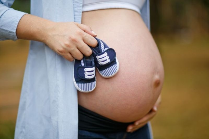 Nahé brucho tehotnej ženy s detskými topánočkami