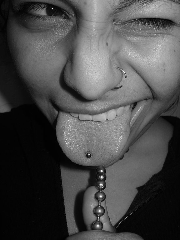 Dievča vyplazující jazyk s piercingom v jazyku a nose